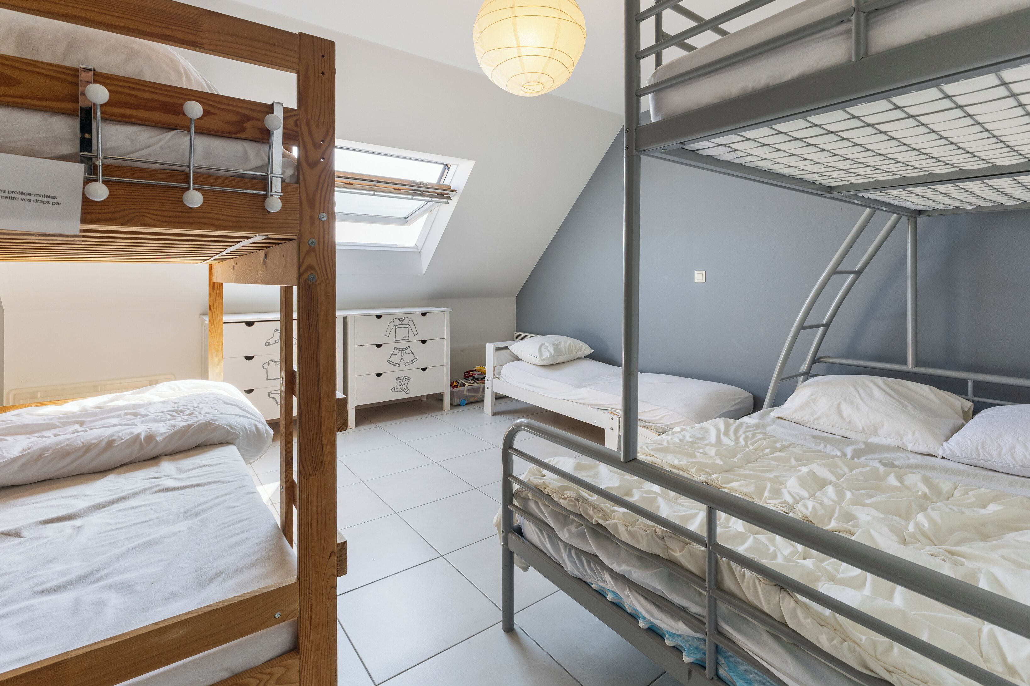 A dormitory room with bunk beds, a small dresser, and a skylight.