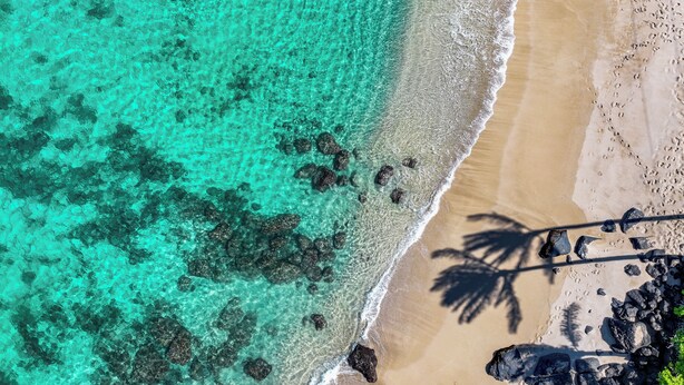 Luchtbeeld van een strand met helder turquoise water, een zandstrand en verspreide rotsen.