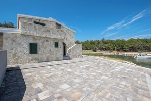 A stone building with a paved patio and a view of a river. - Seaside Oasis on Island Vir With Private Pool and Ocean Views (Vir)