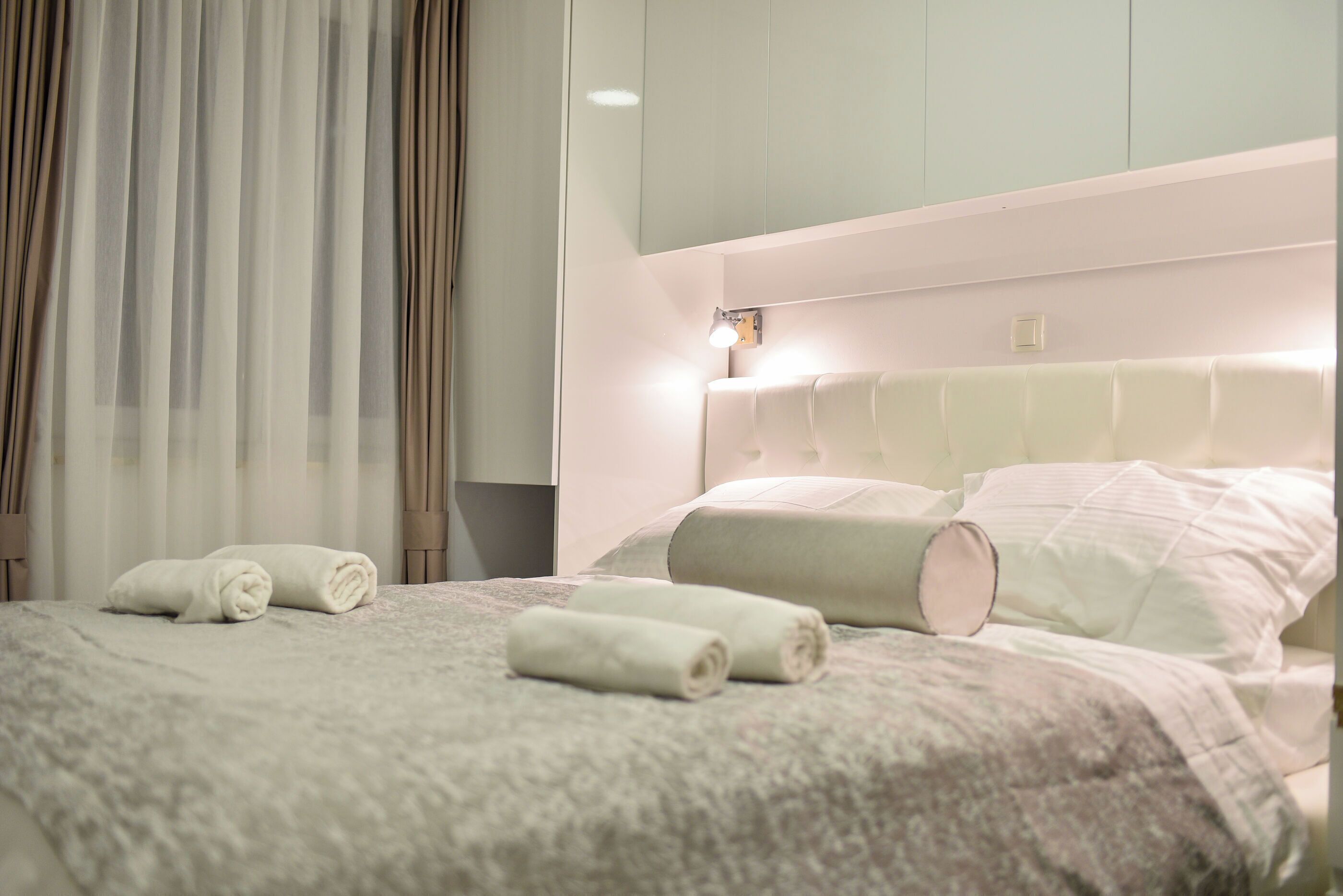 Una cama bien hecha con toallas enrolladas, un cabecero con iluminación integrada y vistas al interior de la habitación.