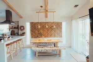 A modern kitchen with a wooden island, bar stools, pendant lights, and a large window.