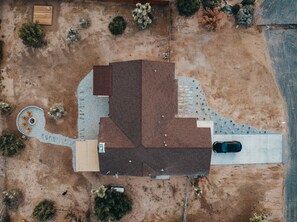 An aerial view of a building with a distinct geometric roof structure, surrounded by sparse vegetation and a paved driveway.