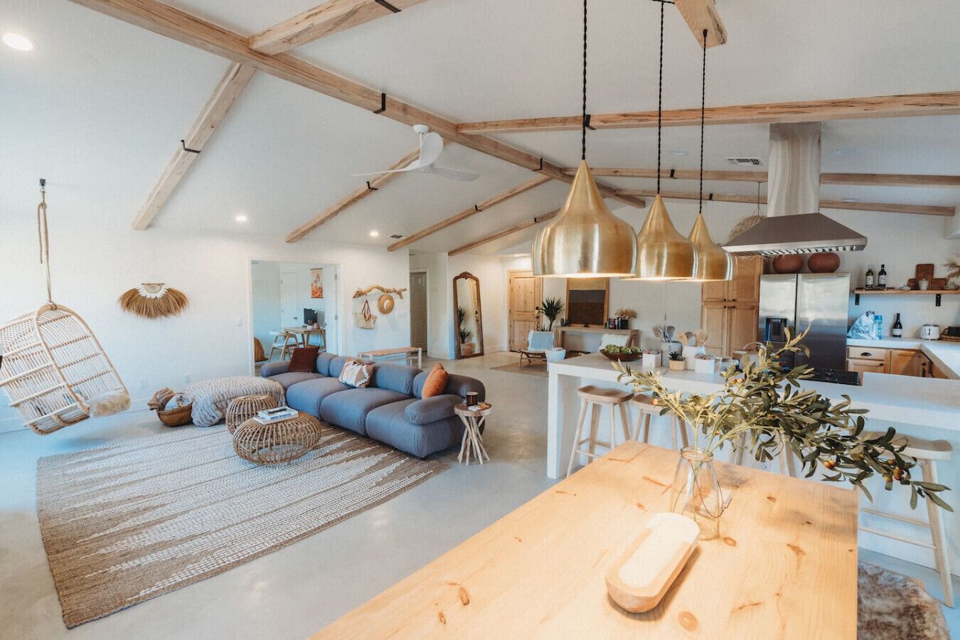 A spacious living area with a large sofa, hanging chairs, and a wooden dining table with a vase of flowers.