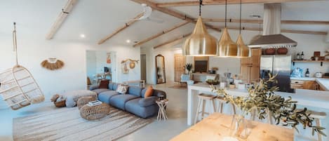 A spacious living area with a large sofa, hanging chairs, and a wooden dining table with a vase of flowers.