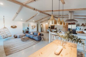 A spacious living area with a large sofa, hanging chairs, and a wooden dining table with a vase of flowers.