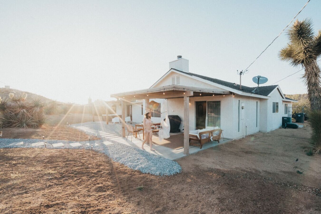 Une maison de plain-pied avec un patio couvert, une antenne parabolique et une allée en gravier.