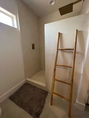 A bathroom with a shower, a wooden ladder, a small rug, and a light switch on the wall. - License To Chill | Pool + Hot Tub | Enclosed Yard (Yucca Valley)