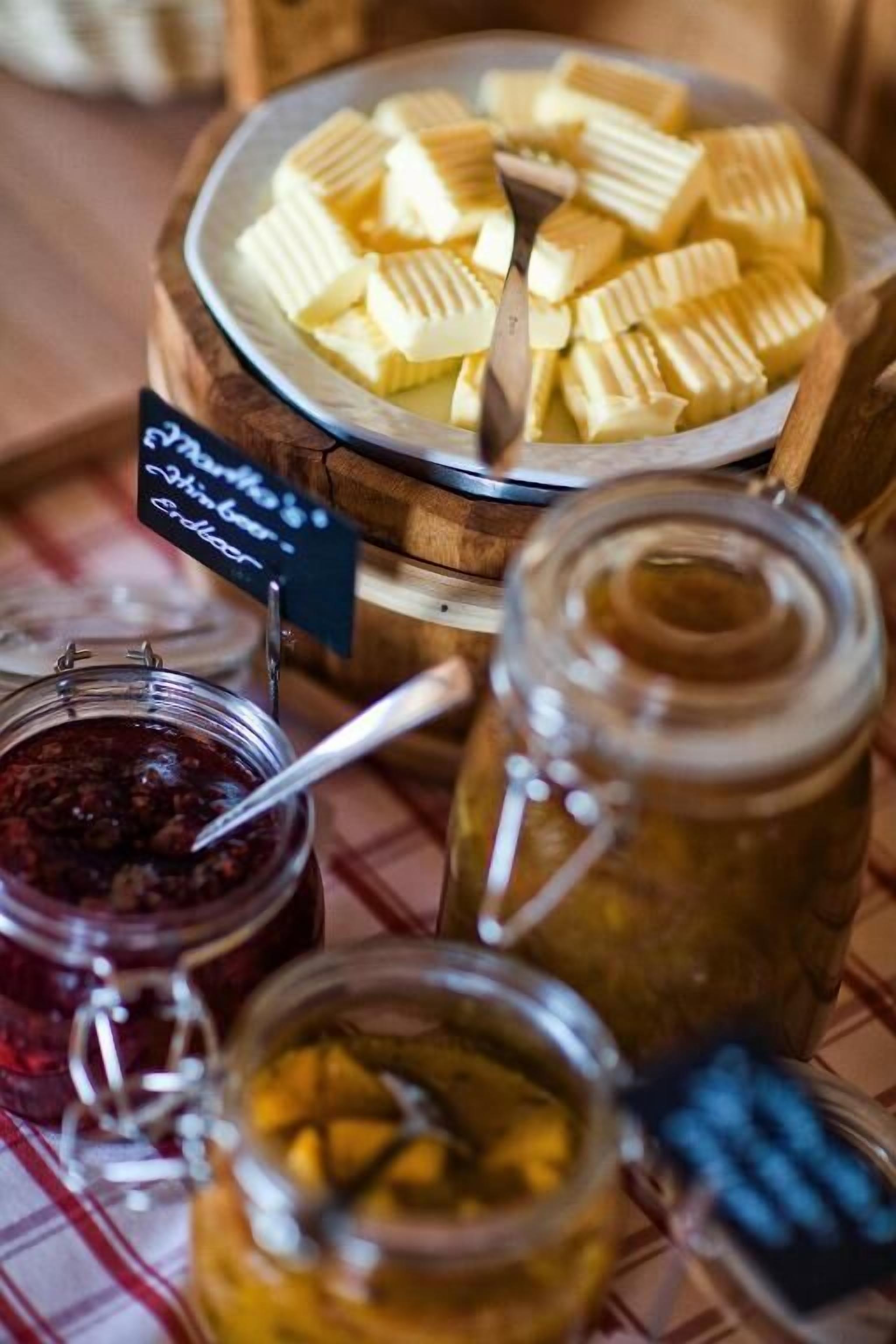 Un bufé con diversos alimentos, entre ellos queso en rodajas, mermeladas y encurtidos.