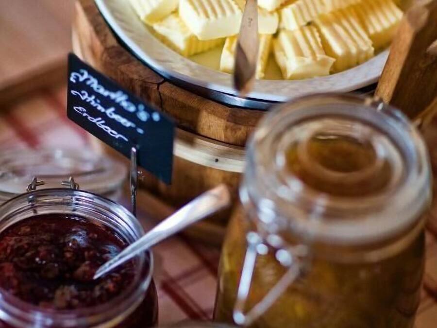 Un bufé con diversos alimentos, entre ellos queso en rodajas, mermeladas y encurtidos.