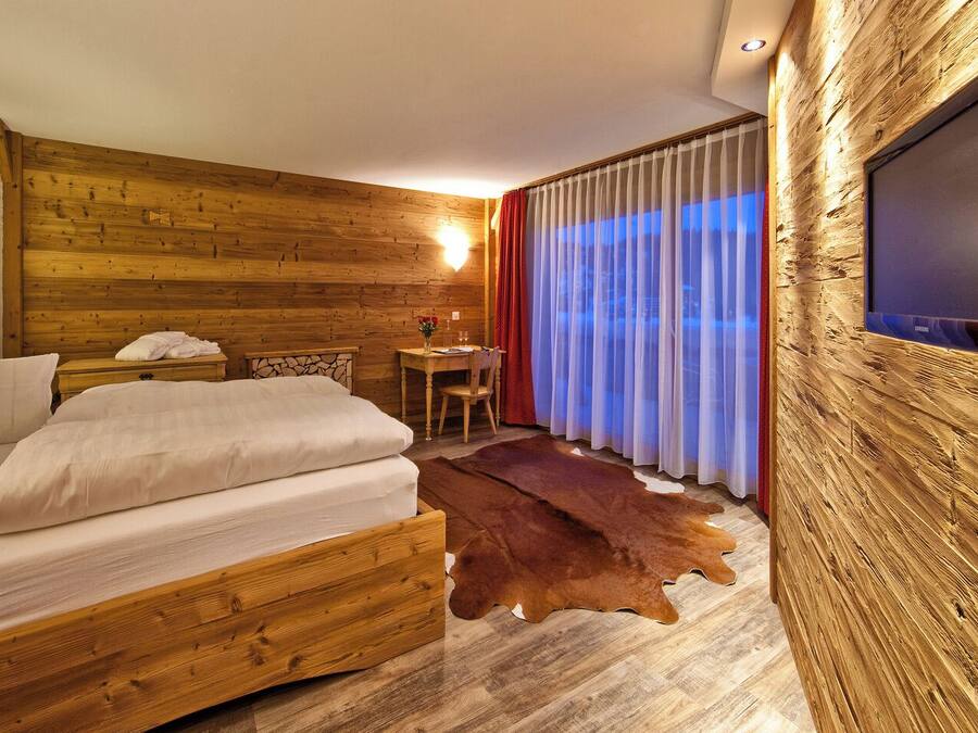 A wooden room with a bed, a small table, and a TV mounted on the wall.