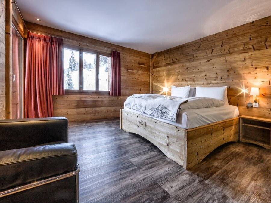 A wooden cabin bedroom with a bed, a chair, and a nightstand.