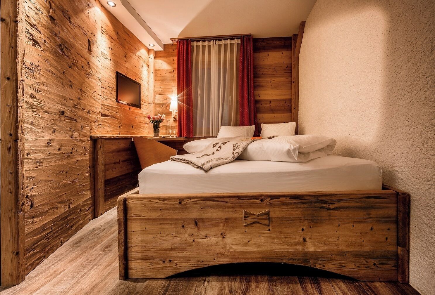 Une pièce en bois avec un lit, une petite table et un téléviseur fixé au mur.