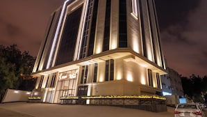 A modern building with a prominent vertical light strip design, a large entrance, and a landscaped area with plants. - Kenanah AlAziziyah (Makkah)