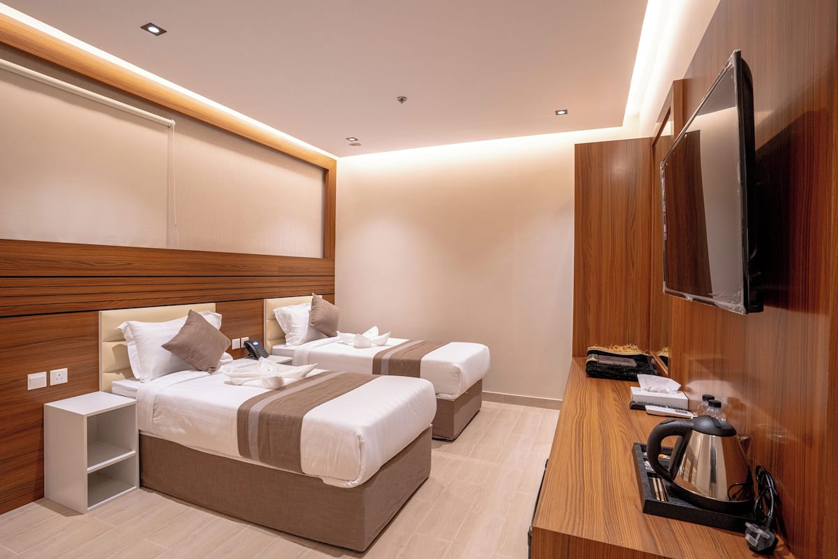 Habitación de hotel moderna con dos camas, cabecero de madera, televisor de pantalla plana, hervidor de agua y una mesita con control remoto.