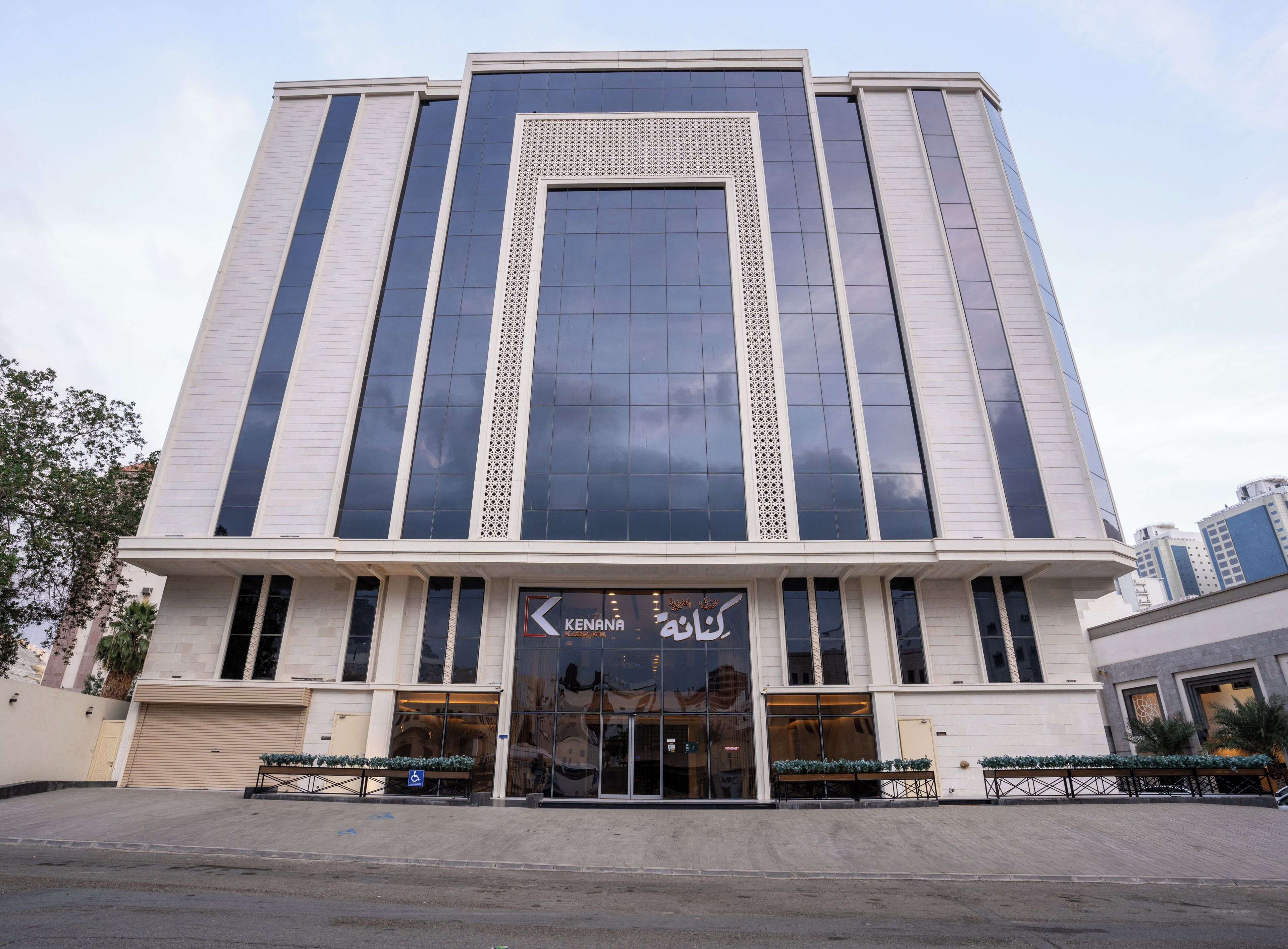 Um edifício moderno com fachada de vidro extensa, uma entrada destacada com uma placa e uma área de estacionamento na frente.