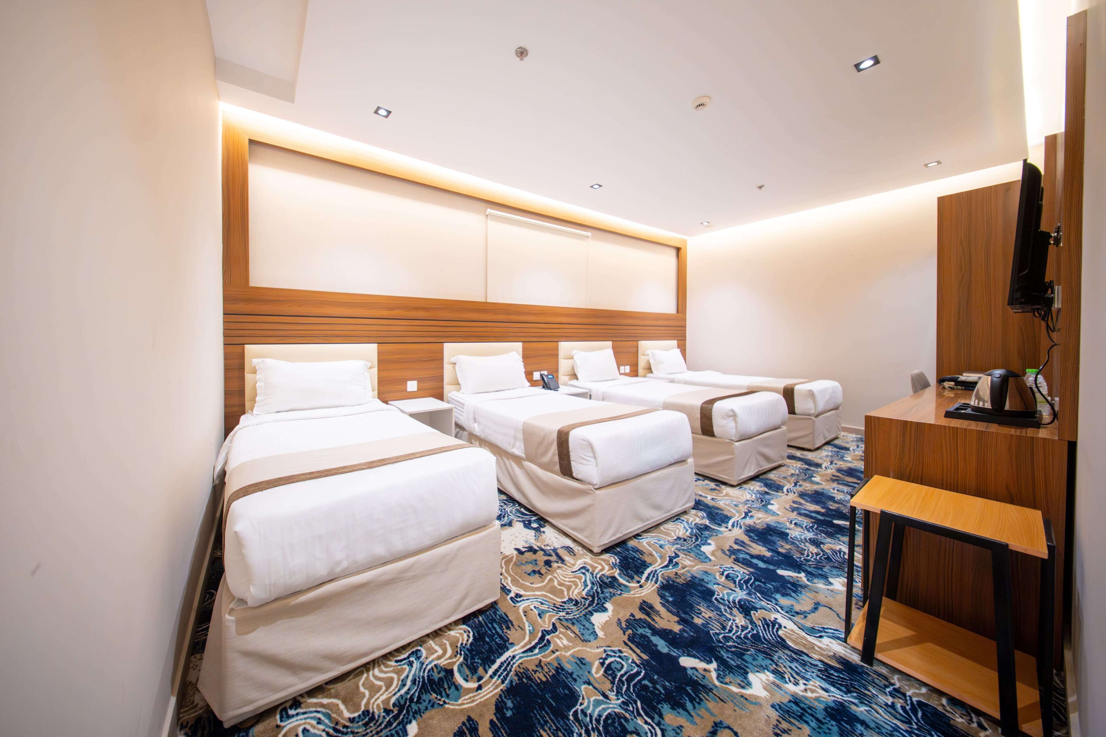 Habitación de hotel con tres camas, un escritorio y un televisor.