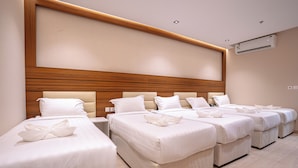 A hotel room with four beds arranged in a row, each with white bedding and pillows. - Kenanah AlAziziyah (Makkah)
