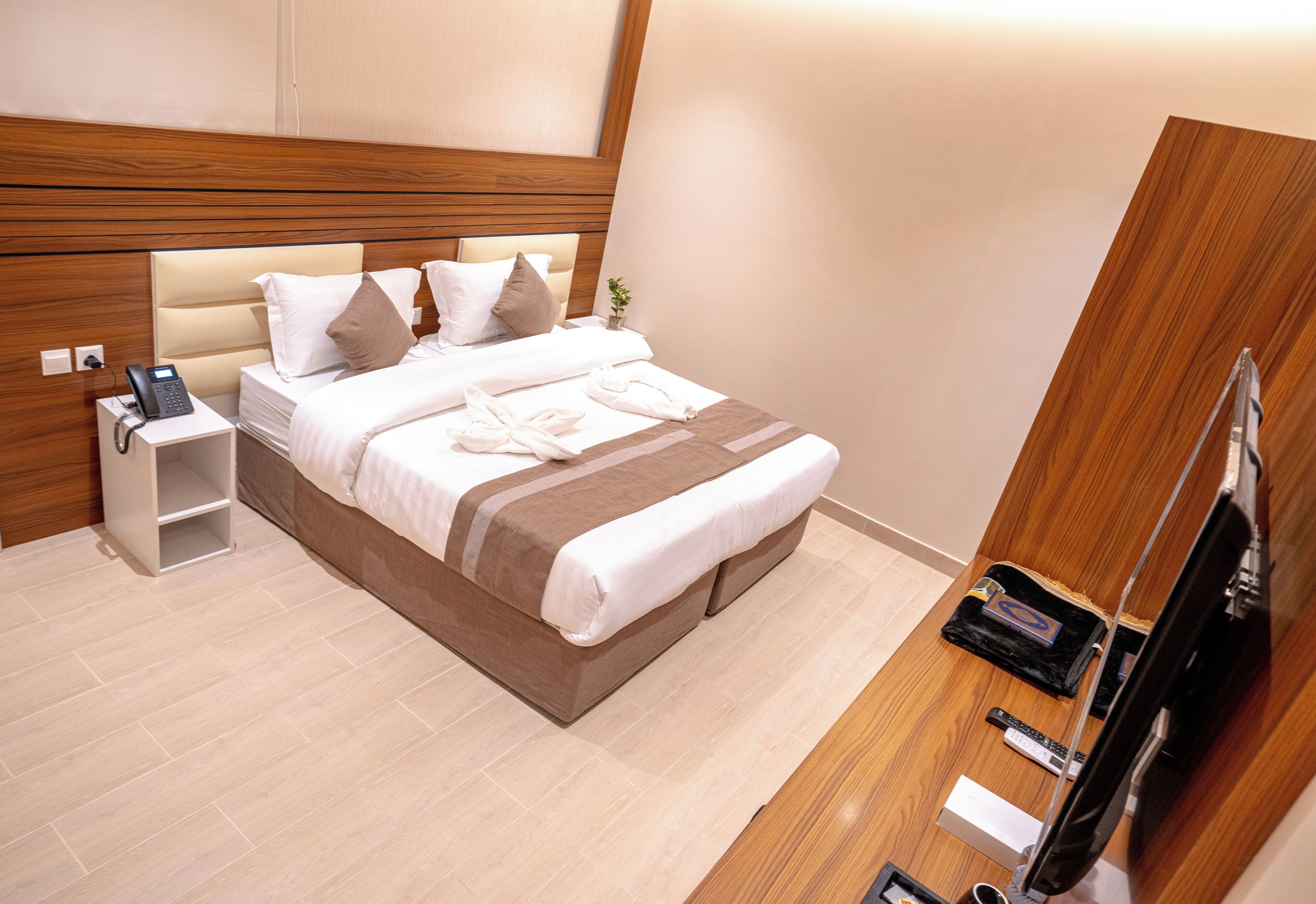 A modern hotel room with a large bed, bedside table with a phone, and a wooden wardrobe.