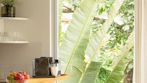 A kitchen with a coffee machine, a bowl of fruit, and a window with a view of greenery. - Palette by RÊVE/2BR Duplex/Art Getaway/Shared Pool (Assagao)