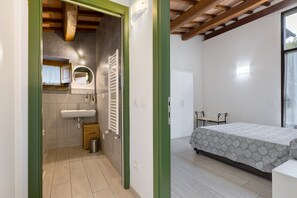 A bedroom with a bed, a window, and a bathroom with a sink and mirror.