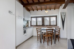 A kitchen with white cabinets, a dining table with four chairs, a window with curtains, and a wall-mounted clock.