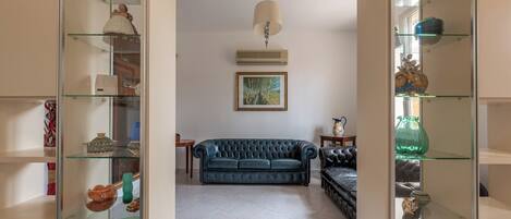 A living room with a blue sofa, glass shelves with decorative items, and a painting on the wall.
