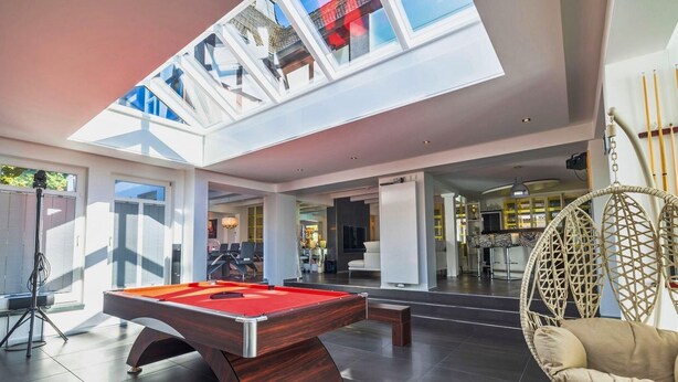 A spacious indoor area with a pool table, a hanging chair, and a skylight.