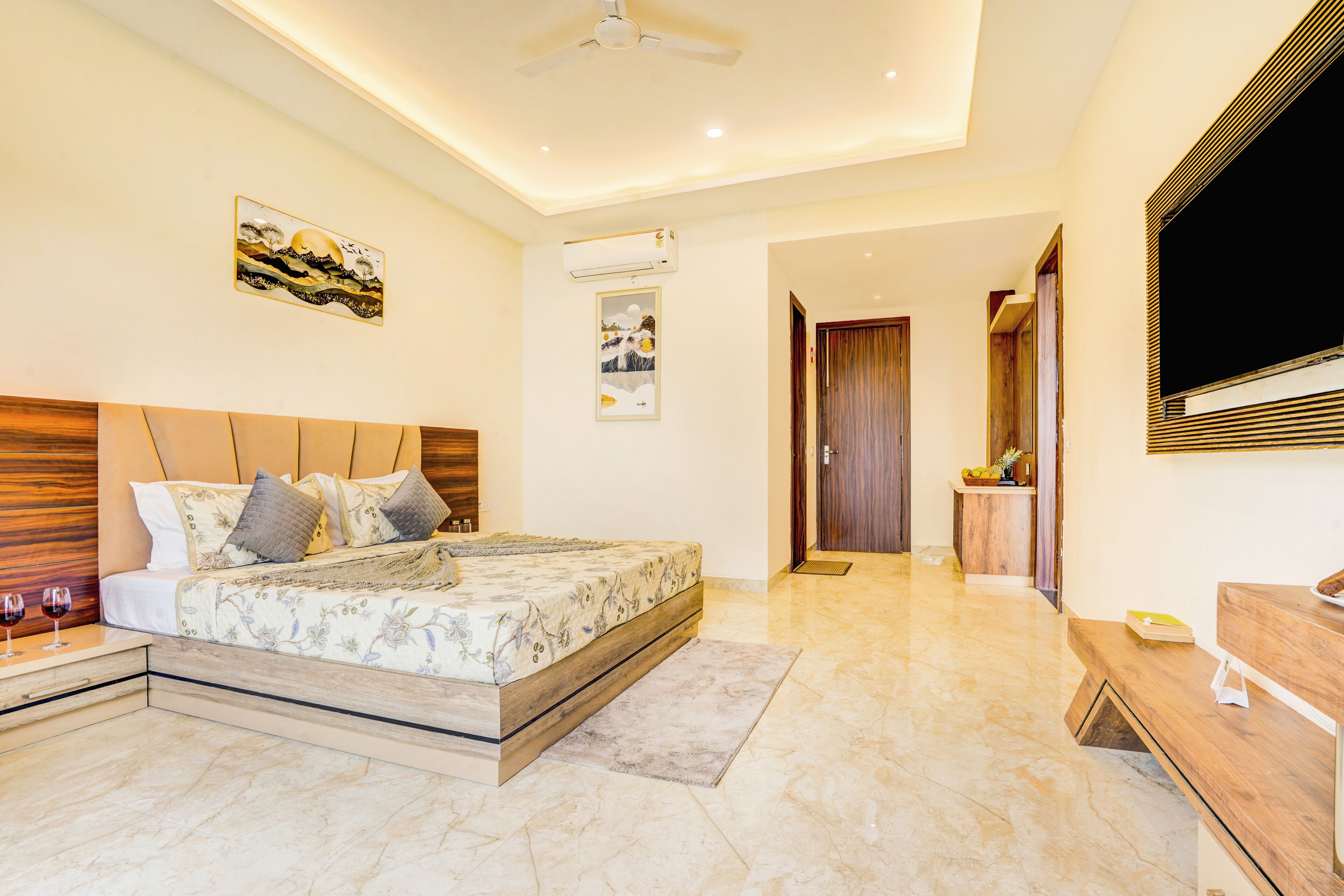 A modern bedroom with a large bed, bedside tables, a wooden headboard, a ceiling fan, and a TV on the wall.