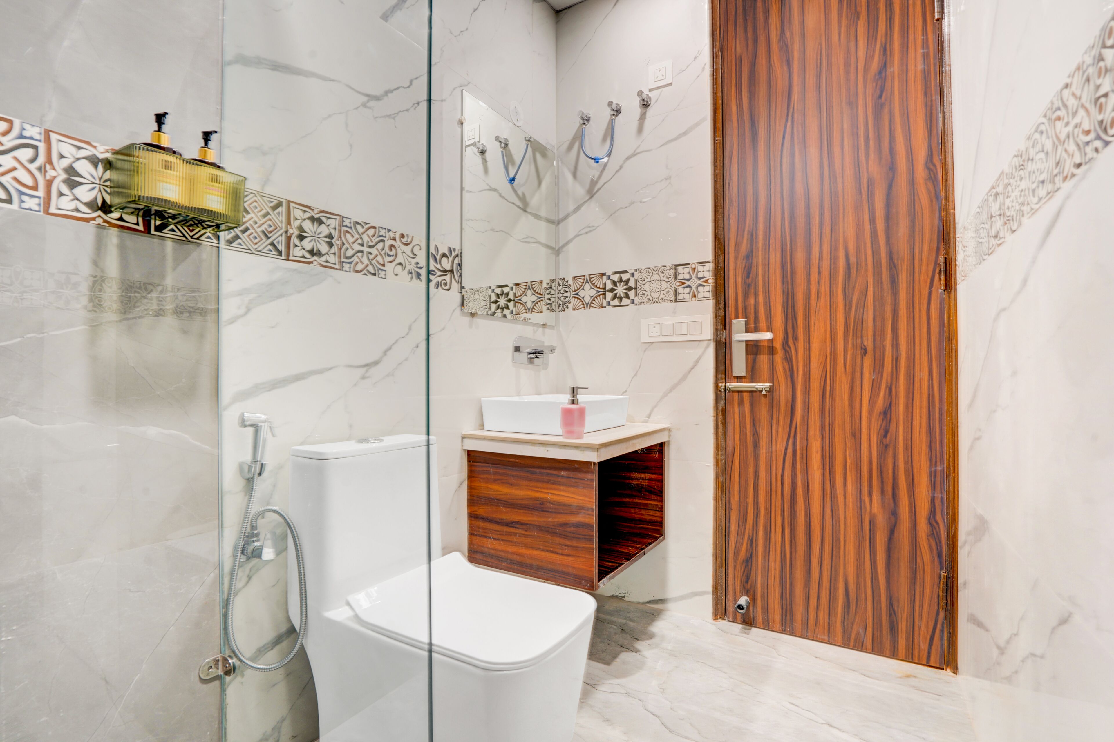 Un baño con cabina de ducha de vidrio, inodoro blanco, tocador de madera con lavabo y una puerta de madera.