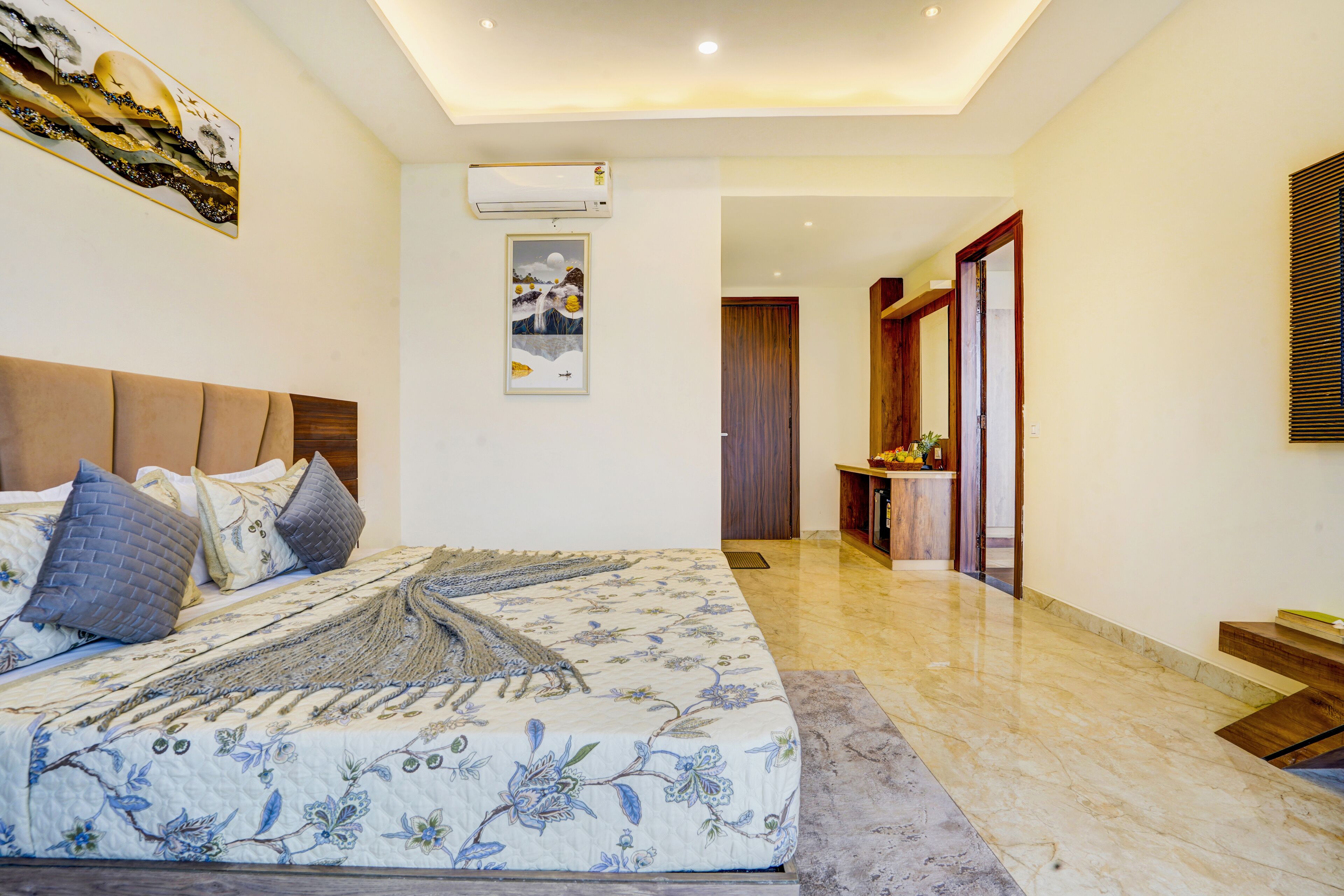 A bedroom with a bed, pillows, a wall-mounted air conditioner, and a door leading to another room.