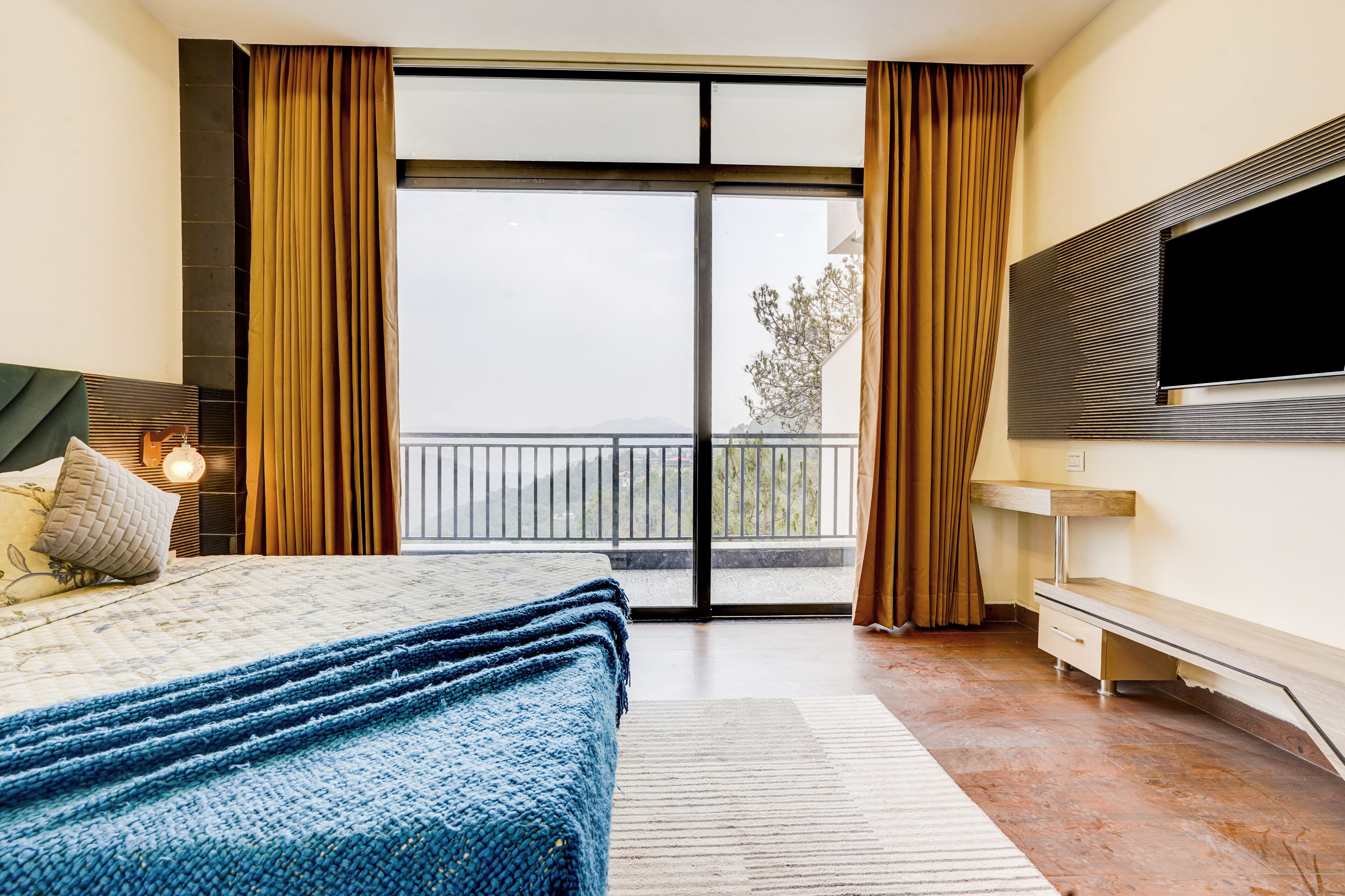 Un dormitorio con una cama grande, un televisor montado en la pared y un balcón con cortinas.