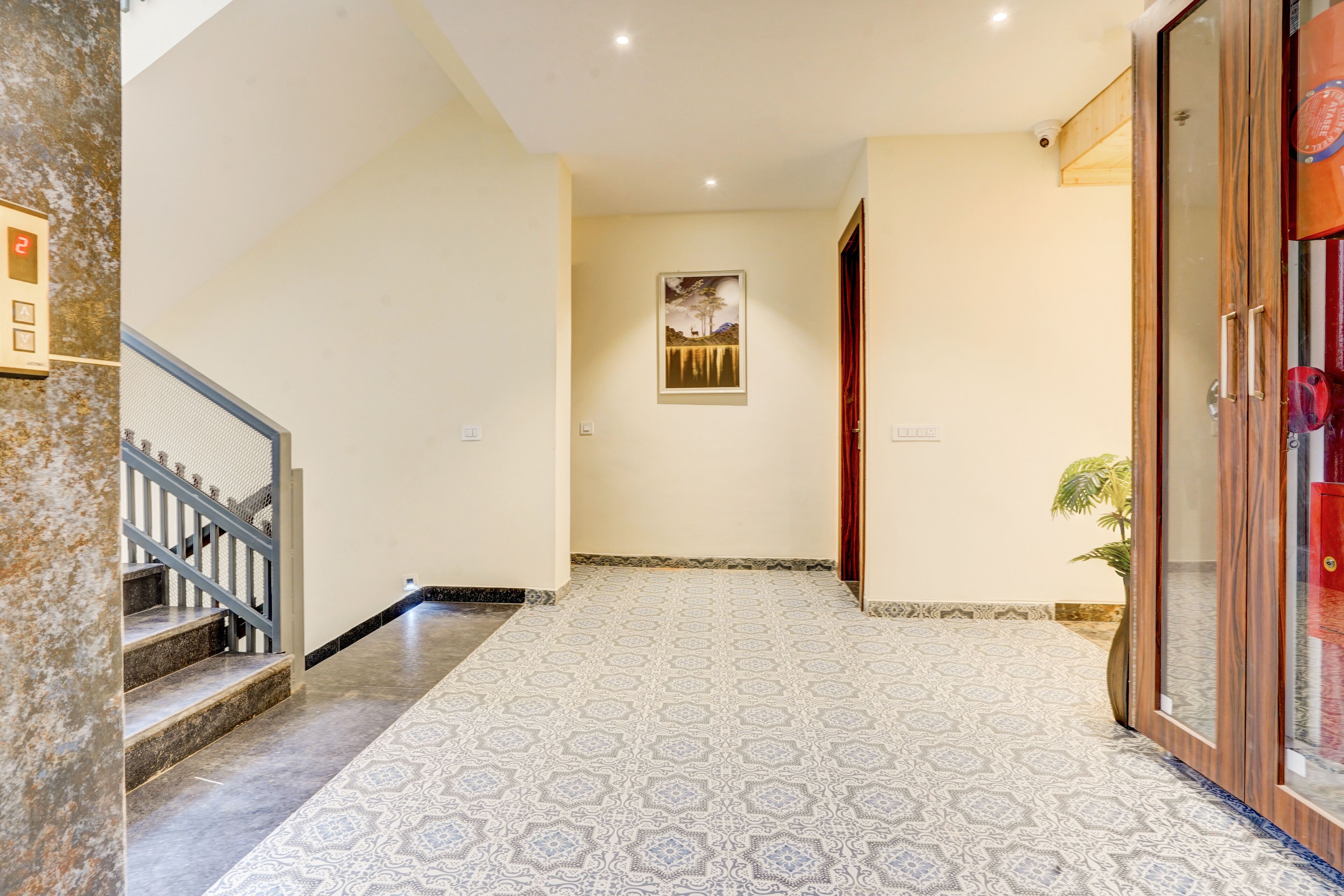 A hallway with patterned flooring, a staircase, a framed artwork on the wall, and a door with a glass panel.