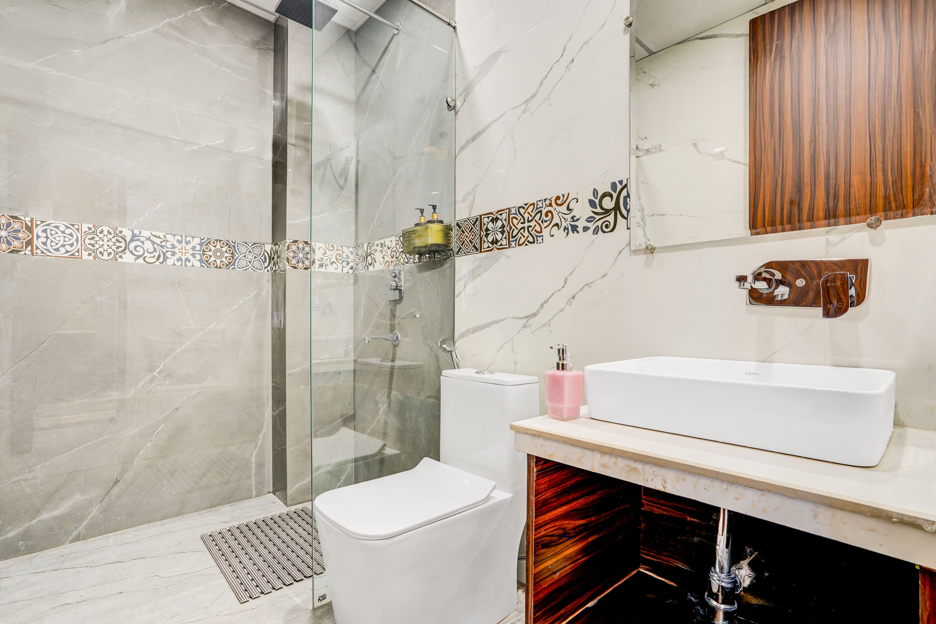 Un baño moderno con cabina de ducha de vidrio, inodoro blanco, tocador con un espejo grande y lavamanos con un mueble de madera arriba.
