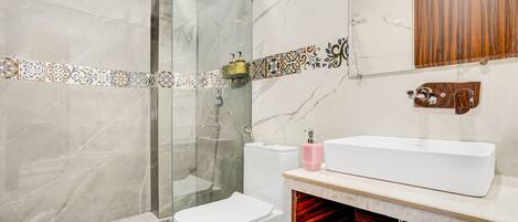 Un baño moderno con cabina de ducha de vidrio, inodoro blanco, tocador con un espejo grande y lavamanos con un mueble de madera arriba.