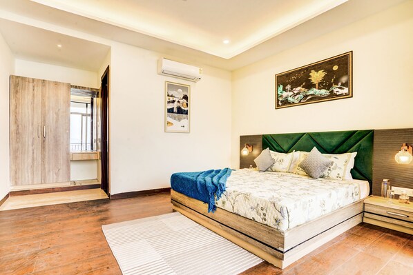 Een slaapkamer met een houten bedframe, een bekleden hoofdbord in groen, een nachtkastje met een lamp en een schilderij aan de muur.