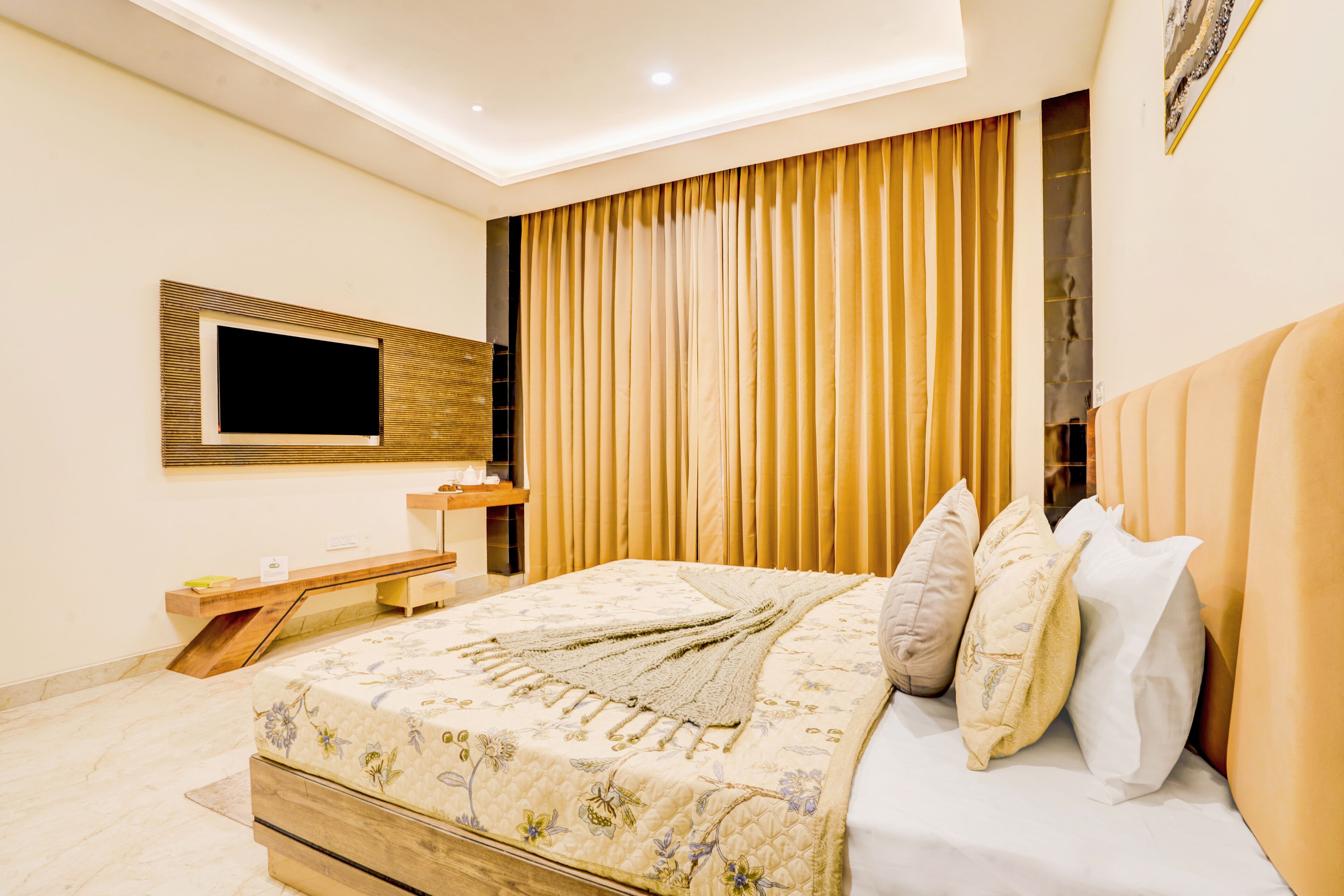 A modern bedroom with a large bed, a bedside table, a TV mounted on the wall, and a curtain-covered window.
