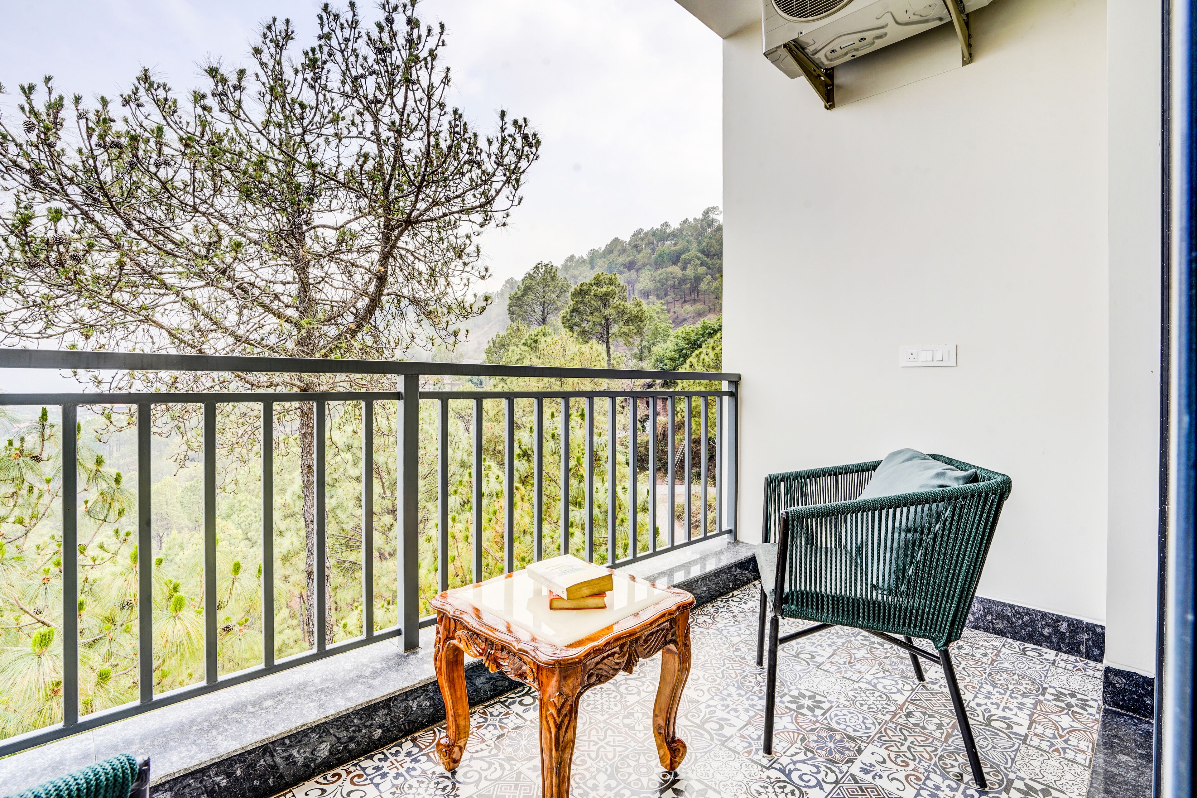Un balcón con una mesa de madera y una silla verde, con vista a un paisaje montañoso.