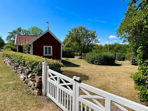 A red building with a white fence, surrounded by greenery and a stone wall.