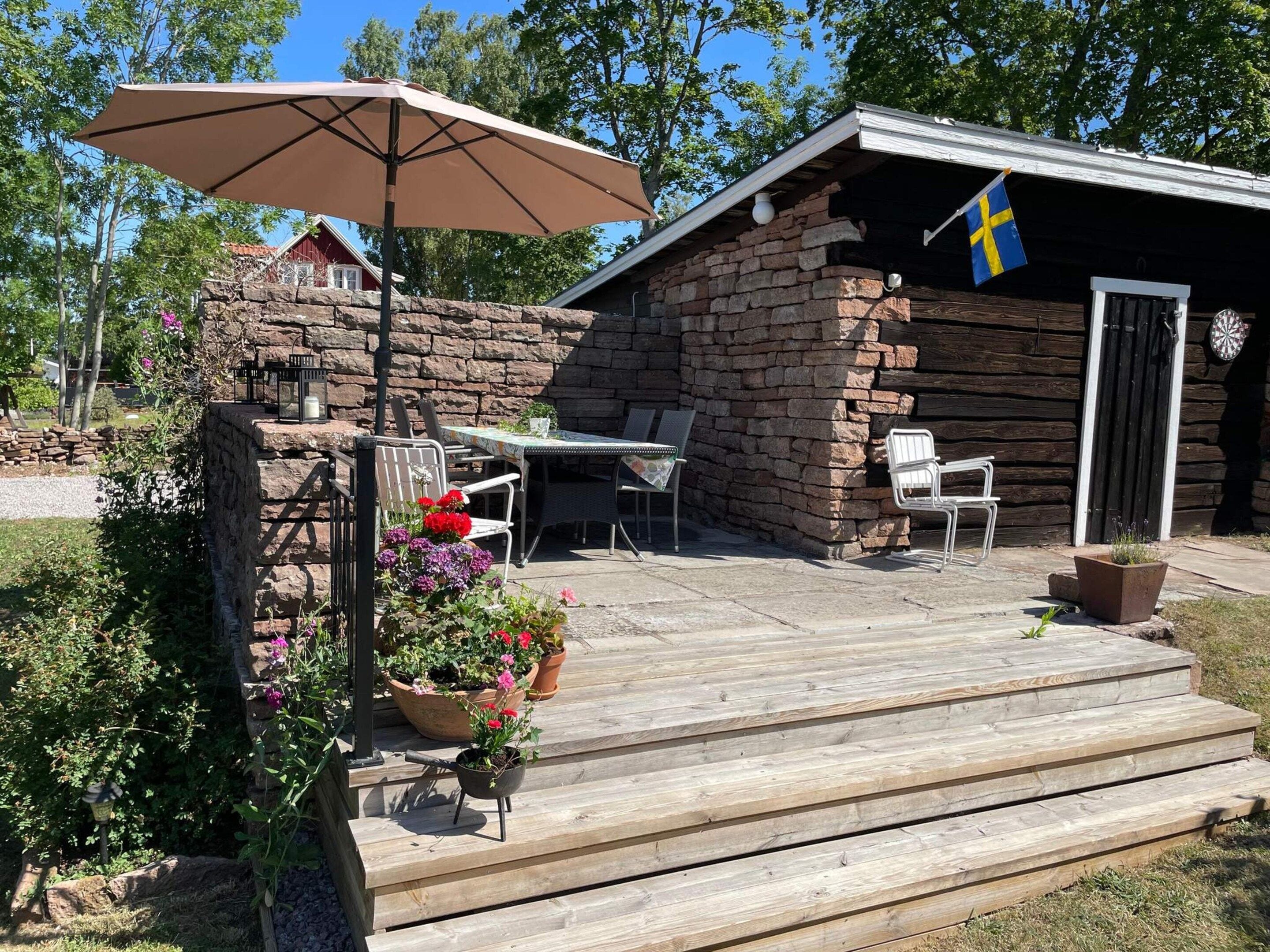 Une terrasse en bois avec des meubles d’extérieur, un drapeau et un mur en pierre.
