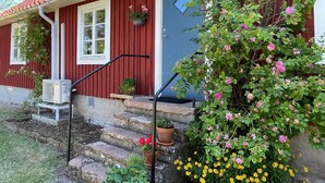 Una casa de fusta vermella amb una porta blava, i escales que condueixen a l'entrada, decorades amb plantes en testos.
