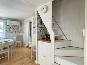 A room with a wooden floor, white walls, a white staircase, and a clock on the wall.