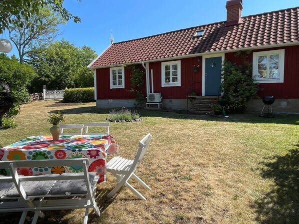 Une maison rouge avec un toit en tuiles, un porche à l’avant et une table entourée de chaises à l’extérieur.