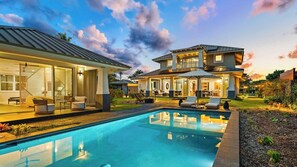 Una casa de dos pisos con piscina, mobiliario de exterior y un jardín cuidado.