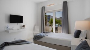 Ein Hotelzimmer mit Bett, Wandfernseher, Nachttisch mit Lampe und einem Fenster mit Vorhängen.