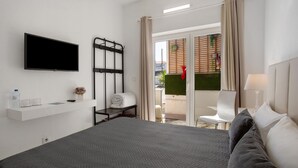 Une chambre d’hôtel comprenant un lit, une télévision, une petite table avec un vase et une bouteille, une chaise et une porte-fenêtre coulissante donnant sur un espace extérieur.