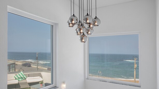 A room with a large window overlooking the ocean, a hanging light fixture, and a view of the beach.