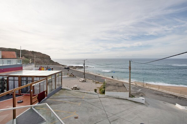 A coastal view from a building overlooking a beach with a road, a parking area, and a cliff.