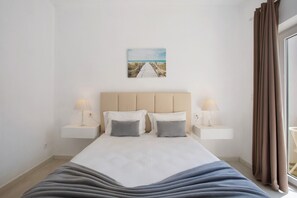 Une chambre à coucher avec un lit, deux tables de chevet, une commode, un tableau au mur et une fenêtre avec des rideaux.