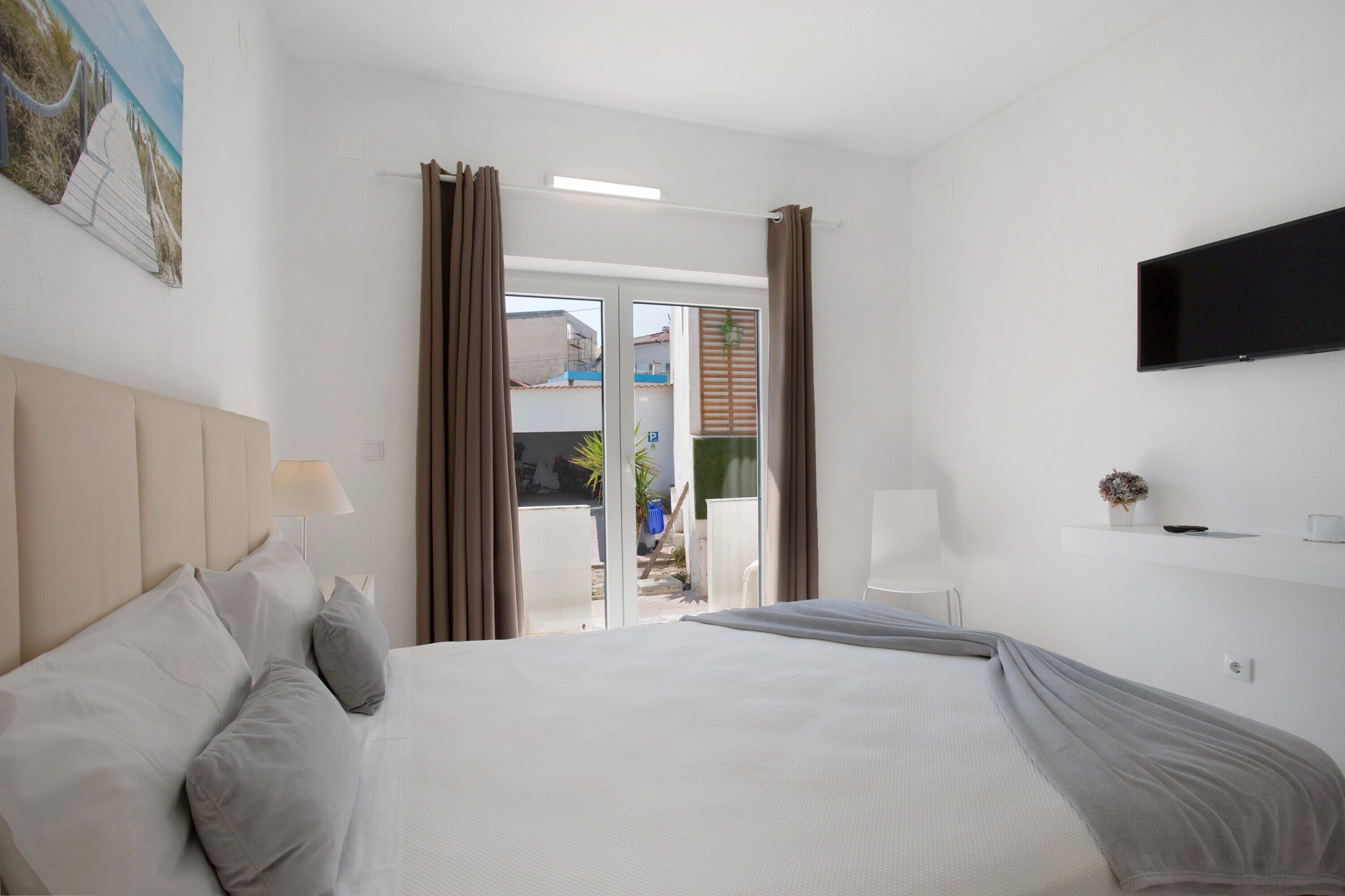 A hotel room with a bed, a television, a window with curtains, and a view of the outside.