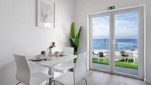 A dining area with a table and chairs, a plant, and a view of the ocean through large glass doors.